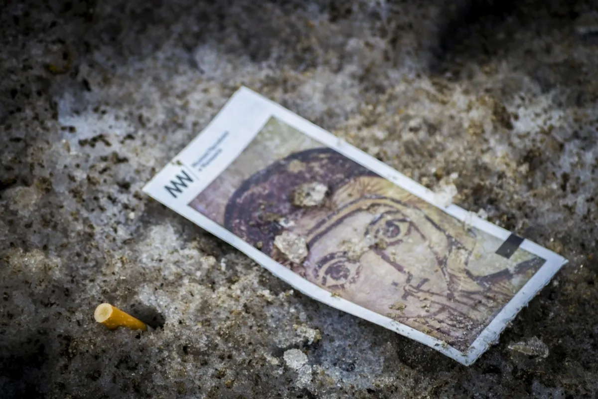 Small holy card lying in dirty snow beside a cigarette filter